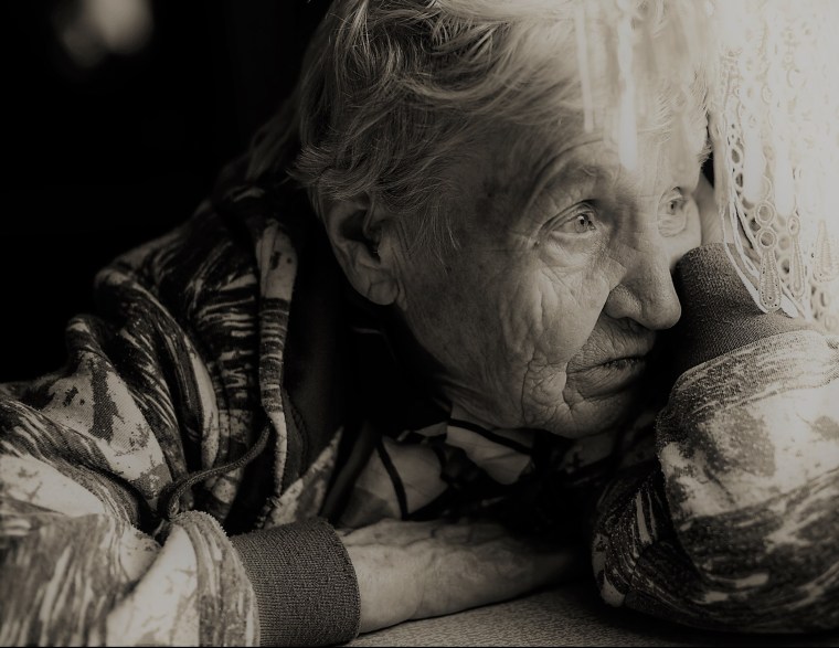 An elderly woman sadly looking out the window.