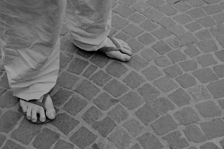 Dirty feet of a man wearing flip flops on the old stone floor. Bologna, Italy