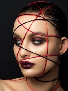 Close up fashion portrait of young beautiful woman with modern trendy makeup. Dark red smokey eyes and lips. Studio shot.