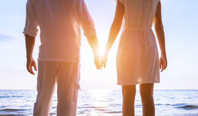Beautiful romantic couple in white clothes holding hands at beach