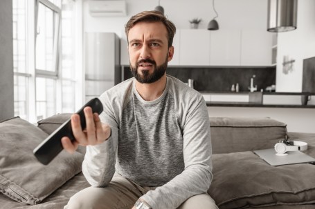 Portrait of a disappointed young man holding TV remote control