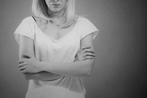 Portrait of an angry woman standing with arms folded on gray background
