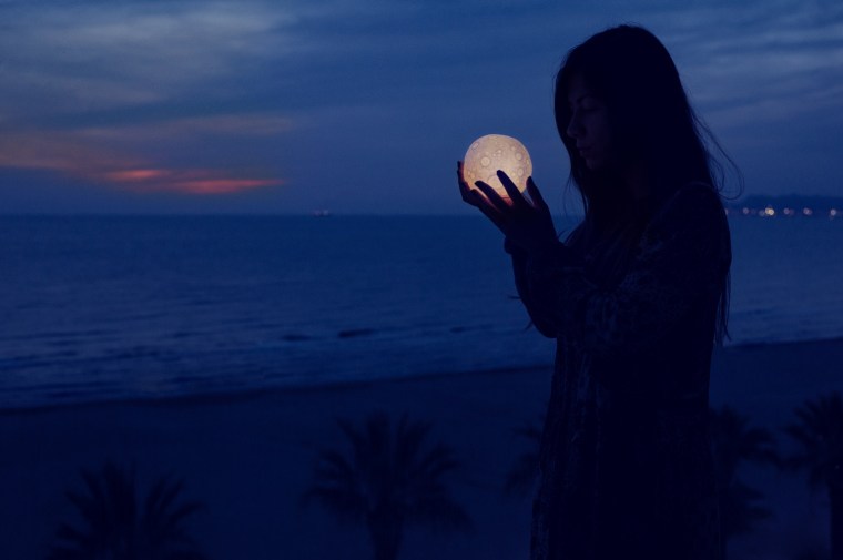 Beautiful attractive girl on a night beach with sand and stars holds the moon in her hands