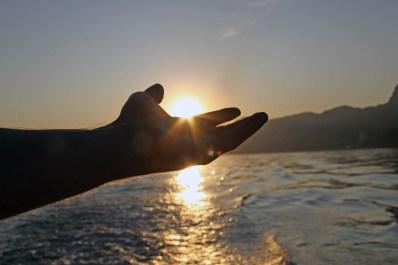 A man reaches out to the sun at sunset on the sea