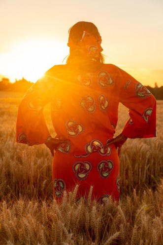African woman in traditional clothes standing in a field of crops at sunset or sunrise
