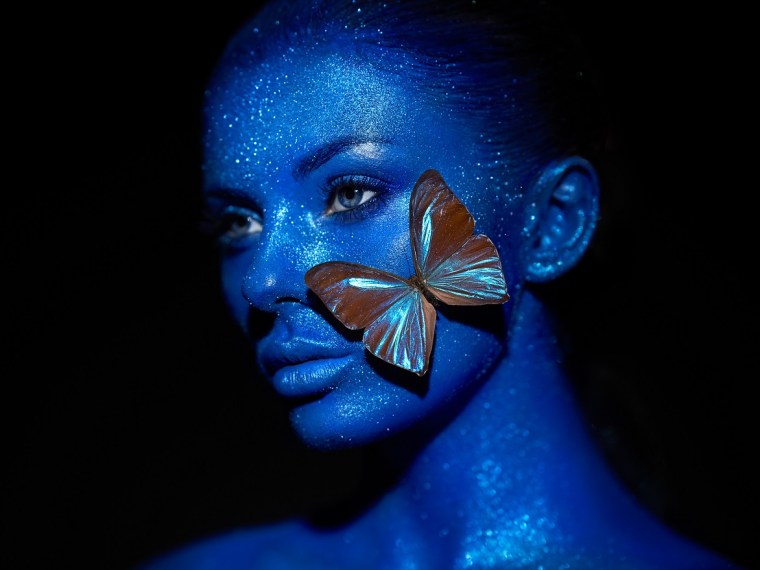 Fashion model woman in blue bright sparkles and neon lights posing in studio.  Portrait of beautiful sexy woman with blue butterfly. Art design colorful glitter glowing make up